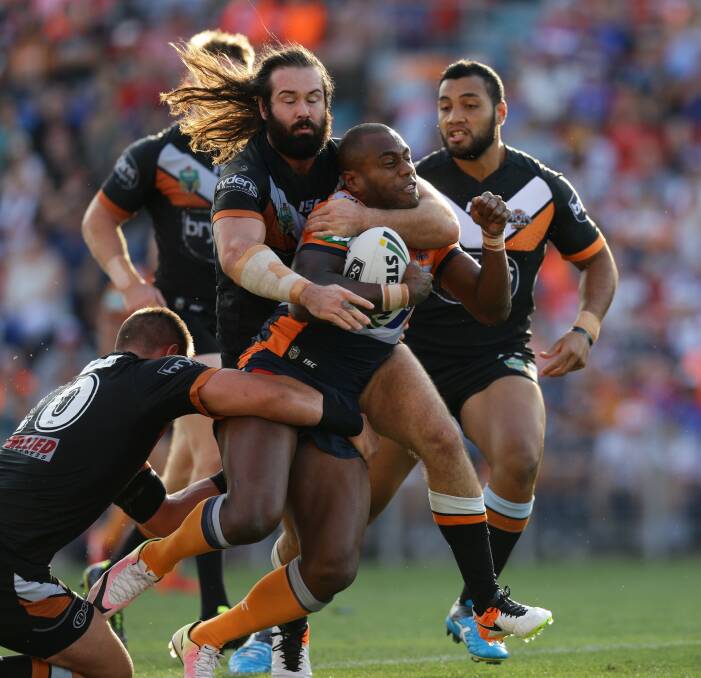 WRAPPED UP: Knights winger Akuila Uate keeps powering ahead despite an attempted headlock from Wests Tigers skipper Aaron Woods. Picture: Jonathan Carroll